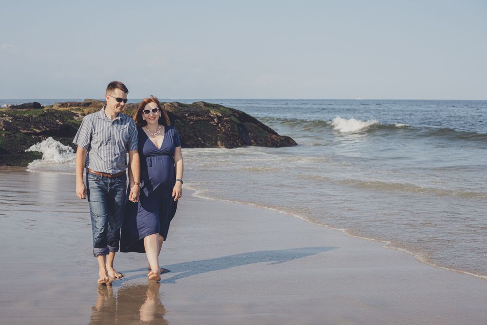 Couple walks along the shoreline of a beach during sunset.