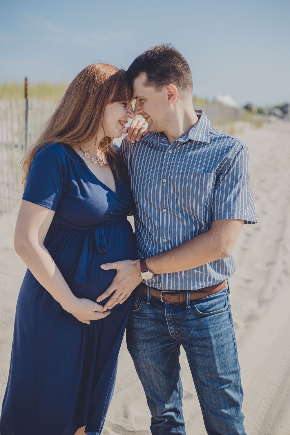 Couple embraces on a sandy beach with ocean waves in the background.