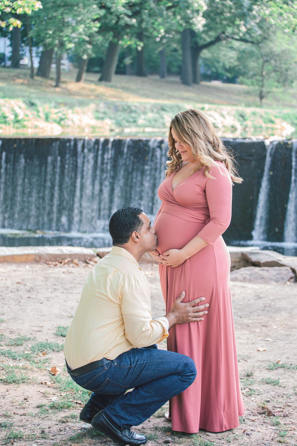 Couple poses together near a waterfall in a park setting during a photo session.