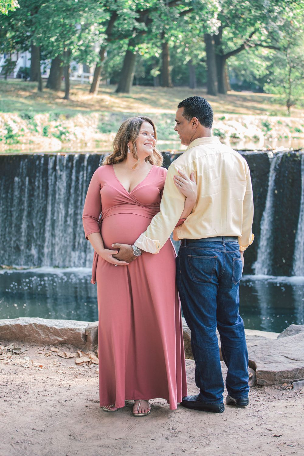 Romantic couple embraces near a cascading waterfall in an outdoor setting.