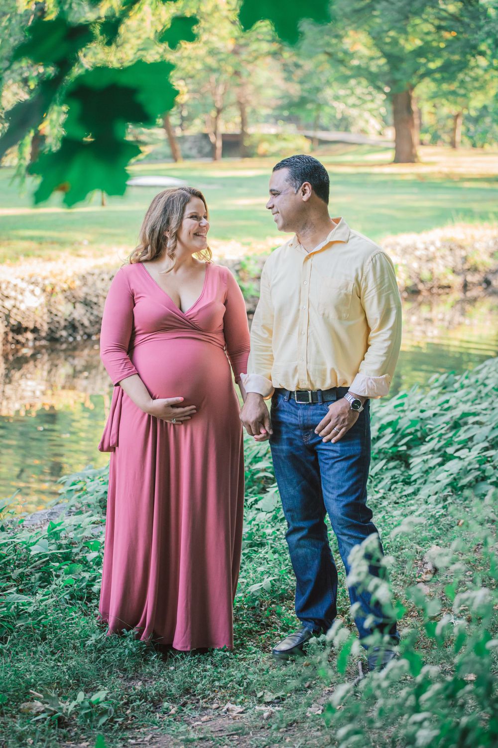 Couple poses together in a lush green park setting during a summer photo shoot.