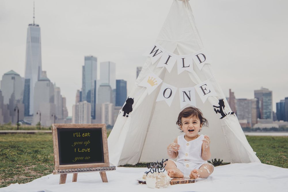 Baby sitting in a teepee tent with NYC skyline visible in background.