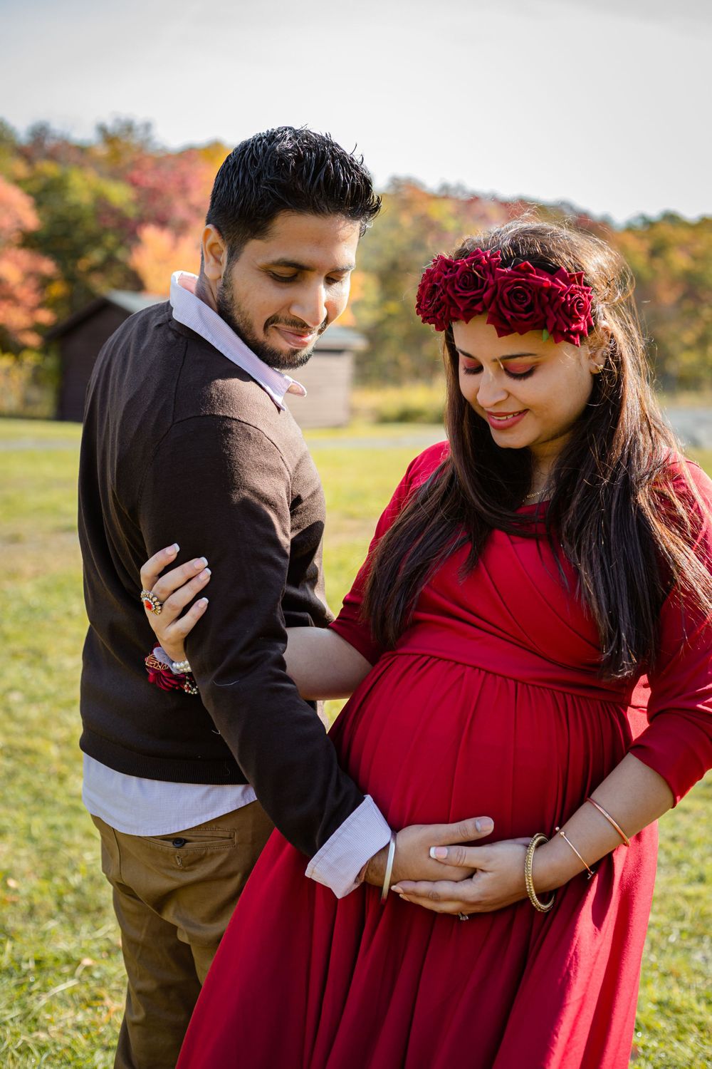 Intimate maternity photos of couple in red dress against autumn landscape.