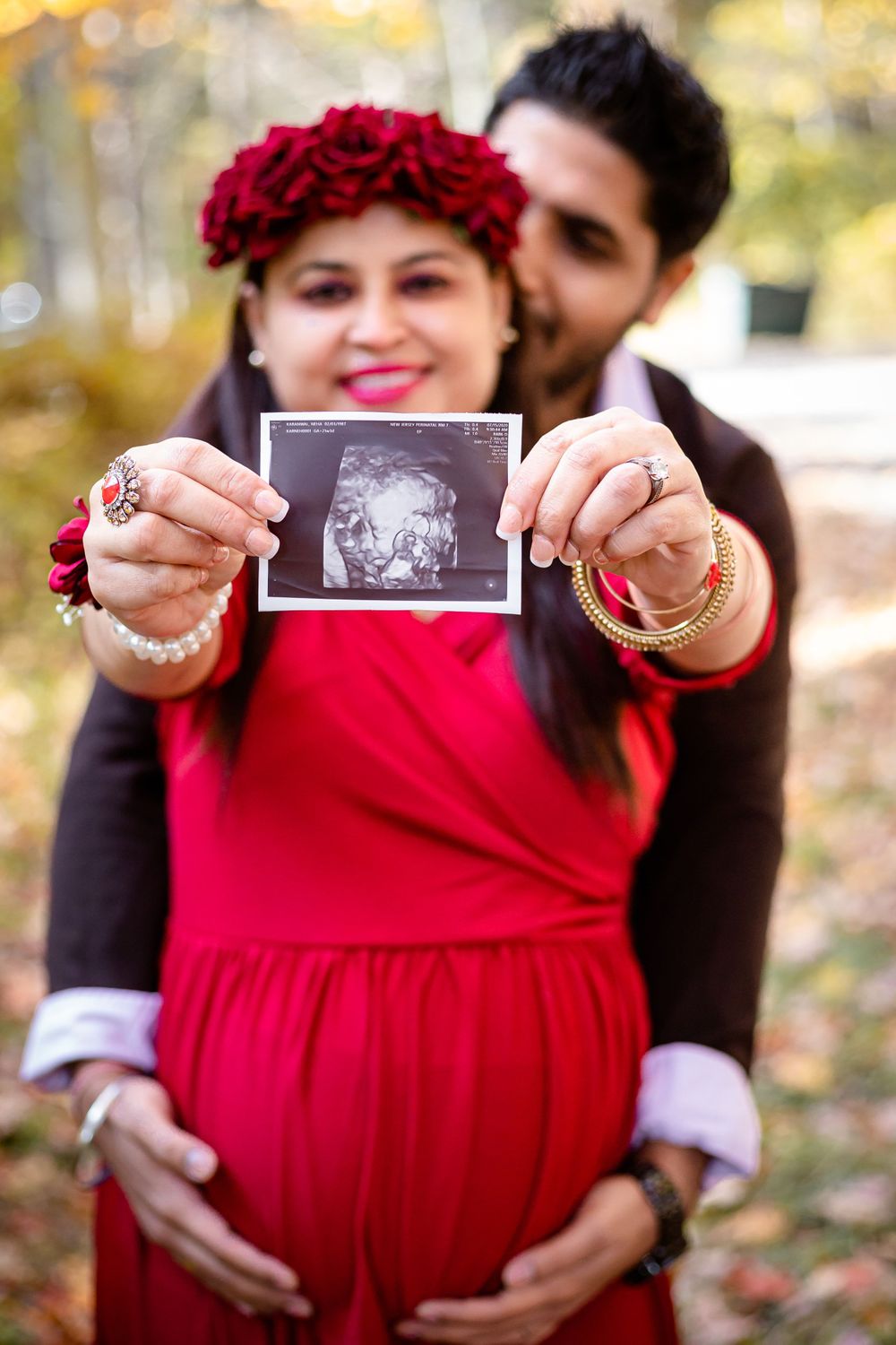 A couple shares a tender moment while holding an ultrasound photo, surrounded by fall colors.