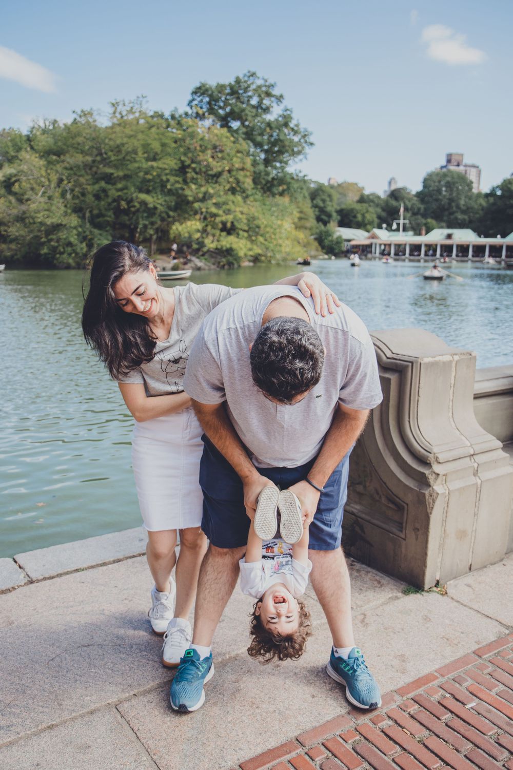 A playful family moment at Central Park lake with a child being held upside down.