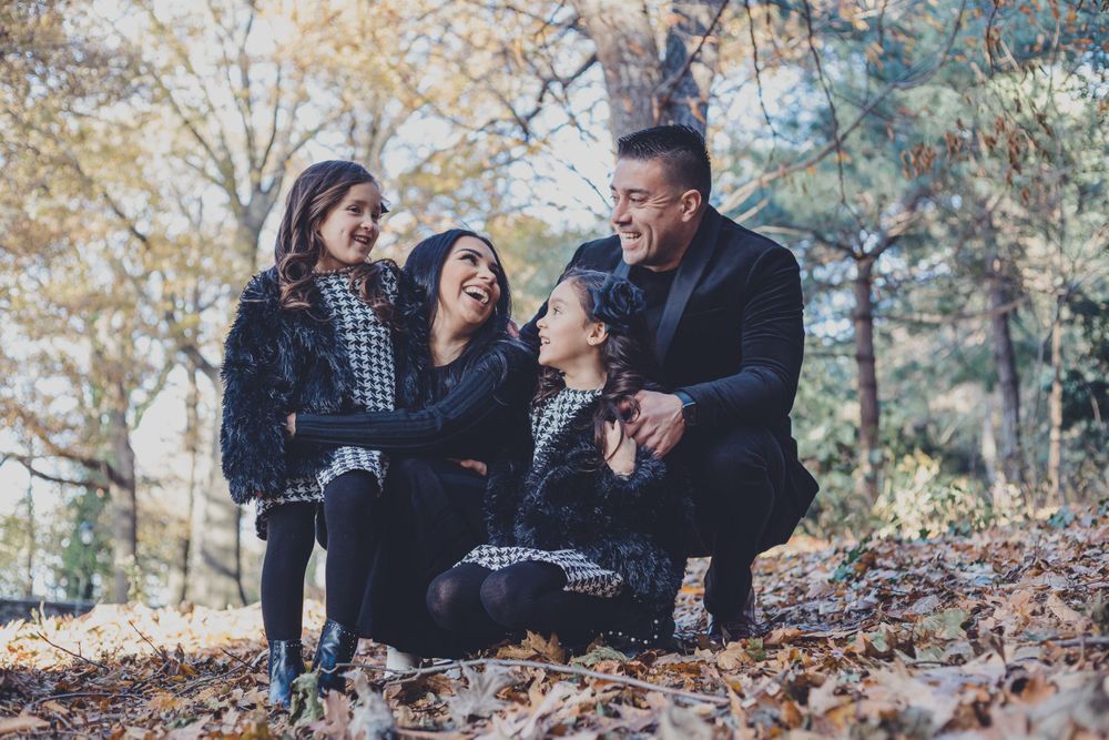 Family laughing together while sitting on fallen autumn leaves in a park.
