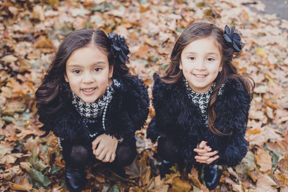 Two children in matching black outfits playing in fallen autumn leaves.
