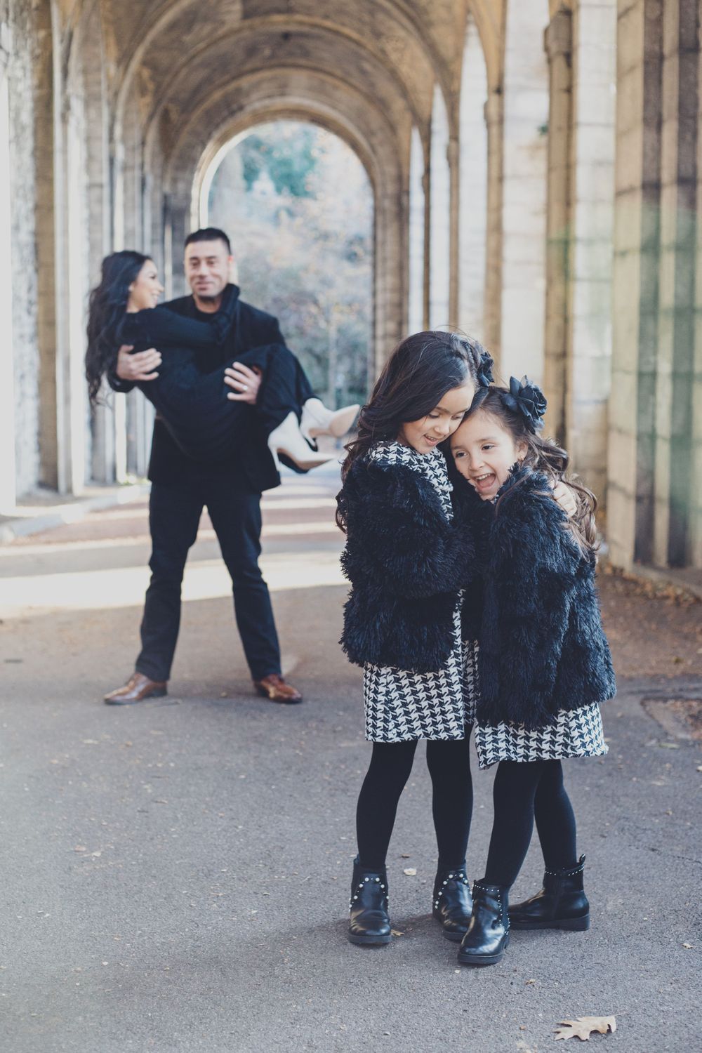 Family poses playfully by stone church colonnade surrounded by fall foliage.