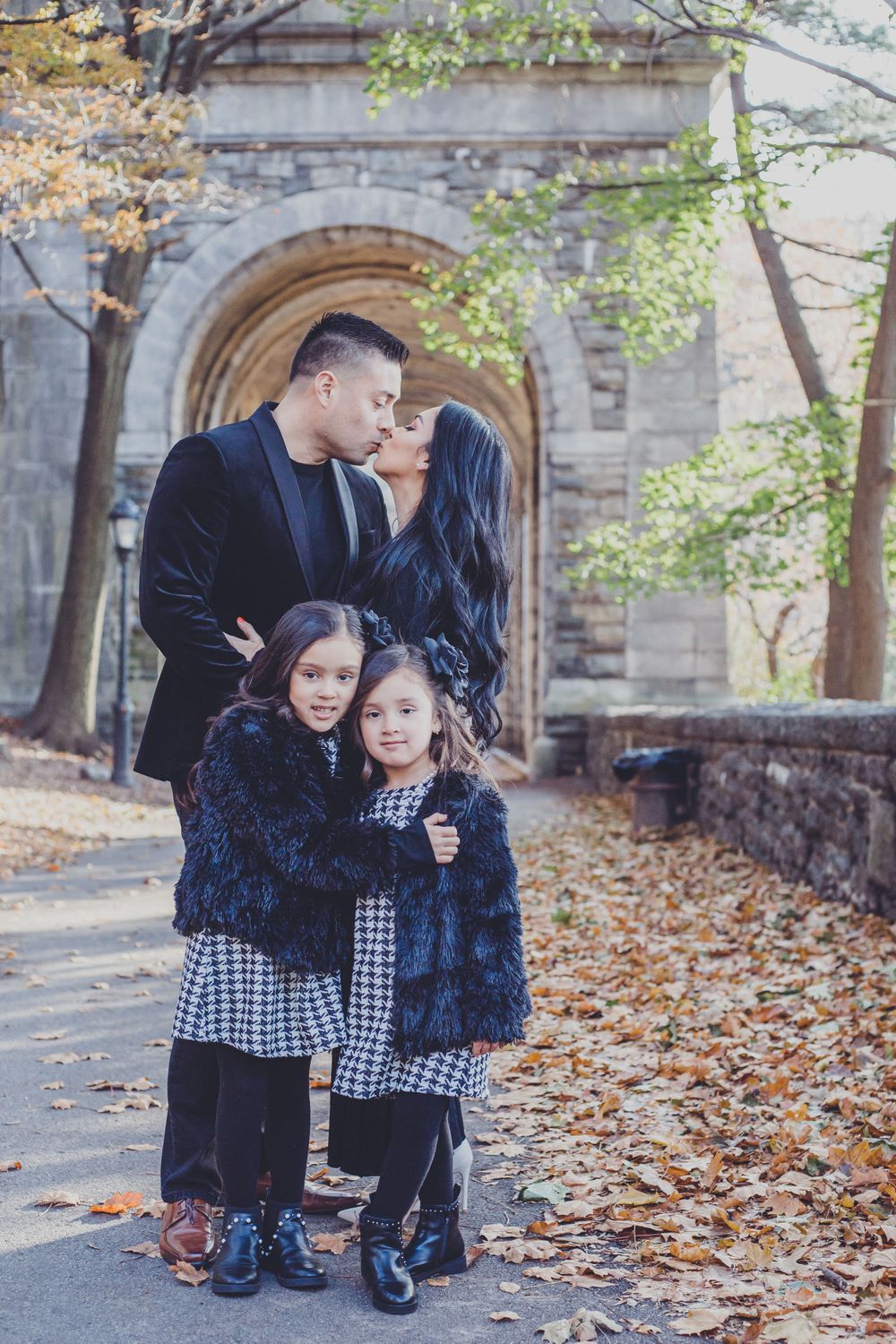 Family autumn photoshoot with fallen leaves and stone archway architecture.
