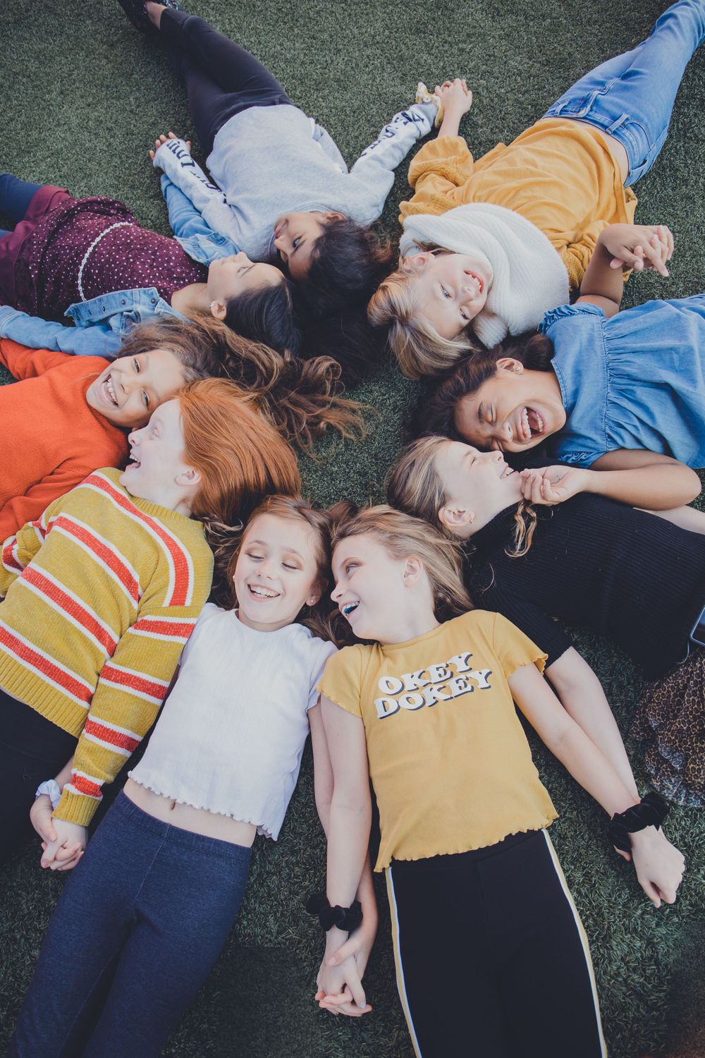 A group lies in a circle on grass wearing colorful casual clothing.