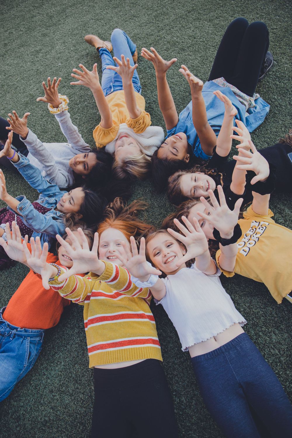 People lay in a circle on grass reaching their arms up towards the camera.