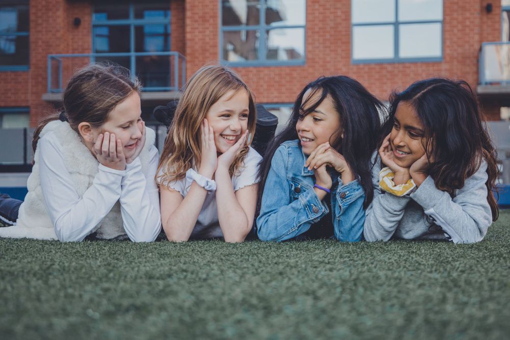 Friends laugh together while laying on grass during an outdoor photoshoot.