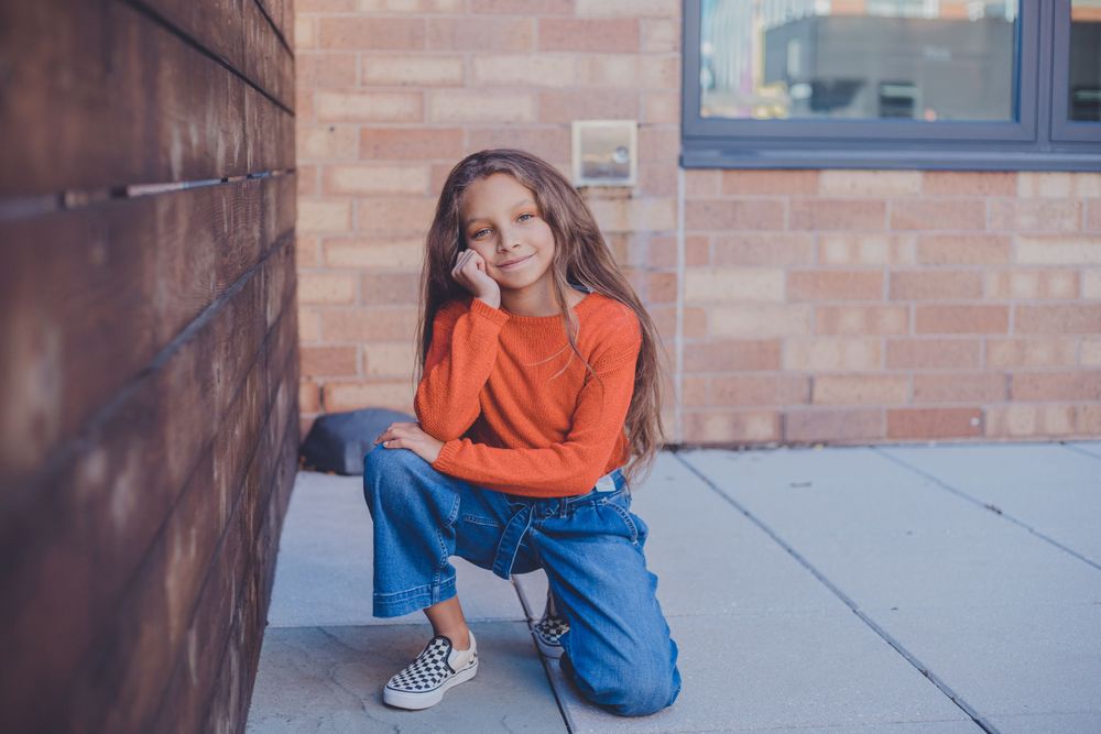 A group sits casually together on a sidewalk near a brick wall.
