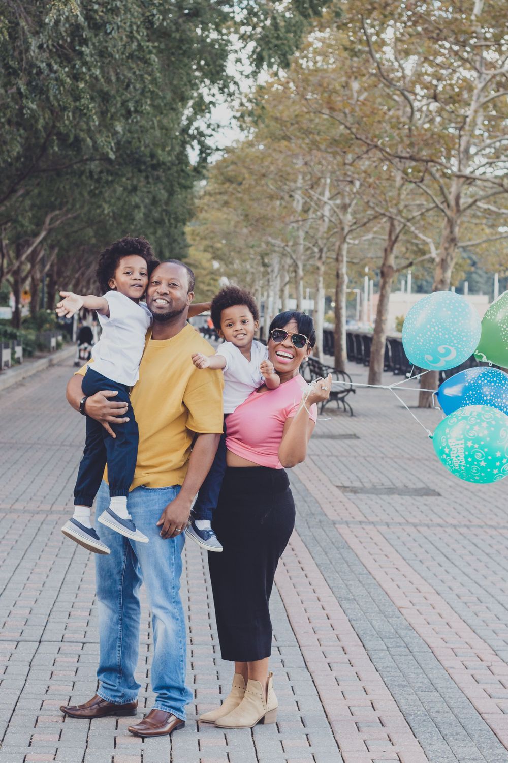 Family enjoying a fun outdoor photoshoot on a tree-lined brick pathway.