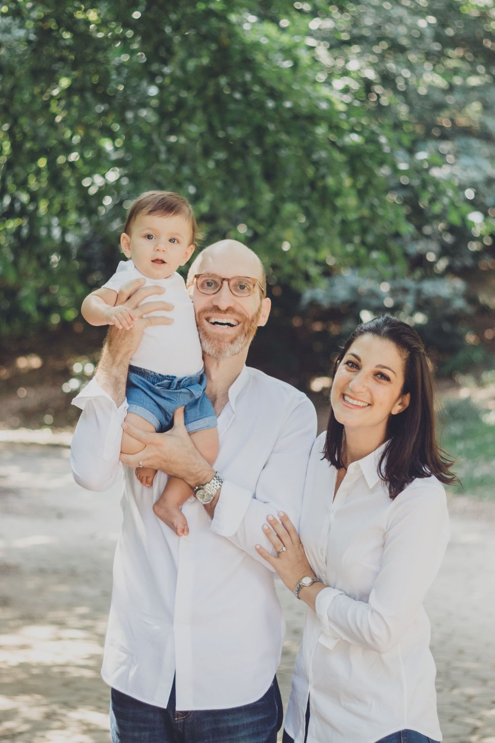 A family wearing matching white outfits poses playfully together outdoors in a natural setting.