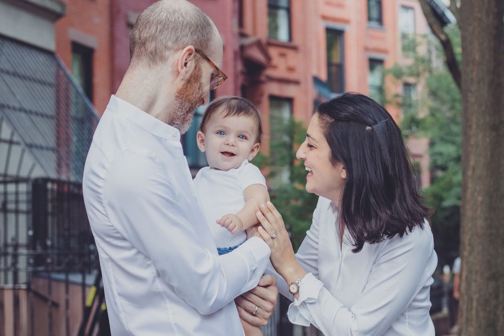 Family sharing tender moments together on urban street with brownstone buildings.