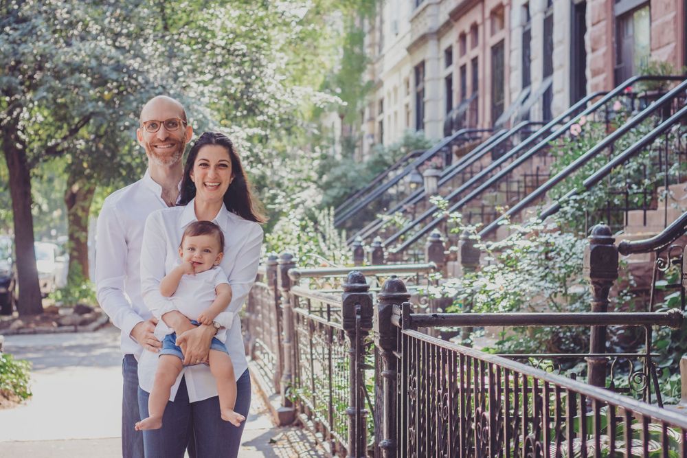 Family portrait session on tree-lined street with classic brownstone architecture.