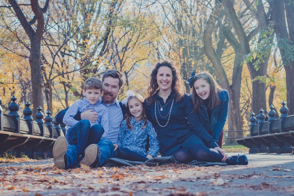 Family photo session in park with autumn foliage and fallen leaves.