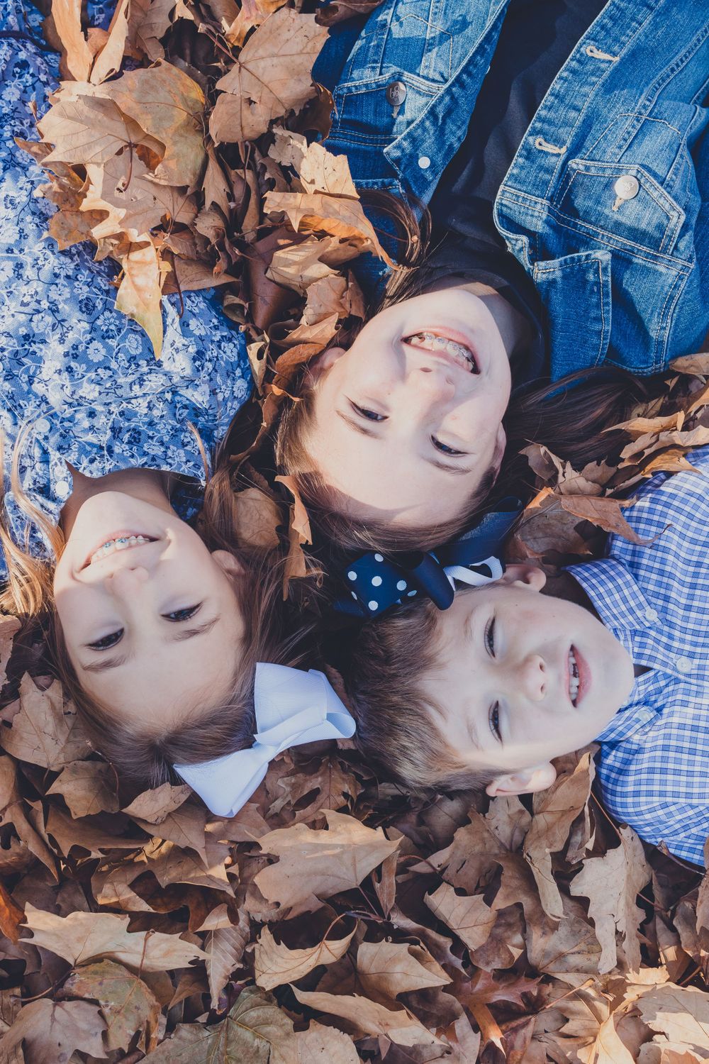 People lying in fallen autumn leaves with joyful expressions.