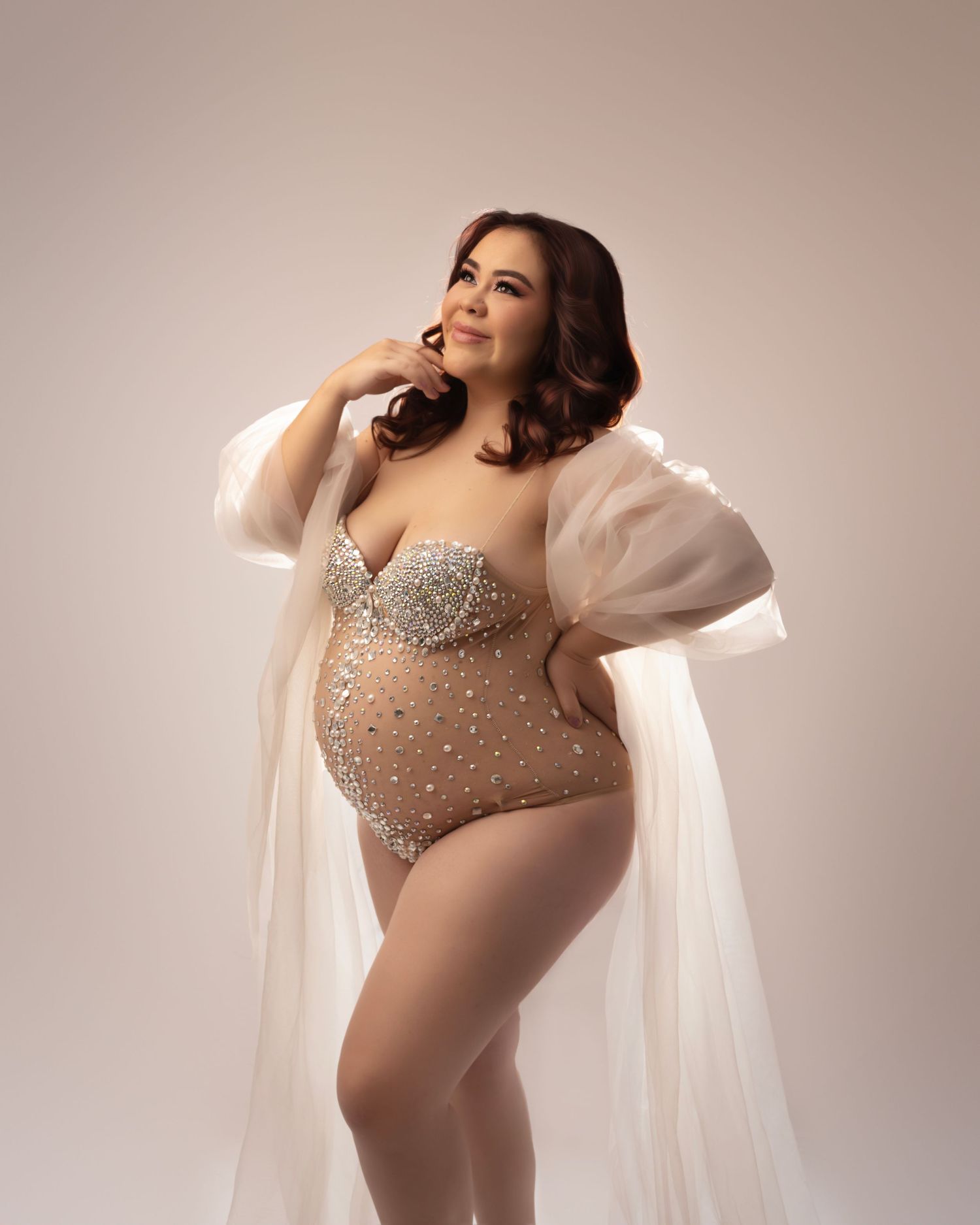 Elegant studio portrait featuring sparkly bodysuit and sheer white robe against neutral backdrop.