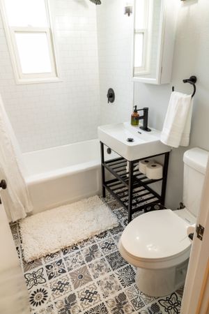 Small bathroom with patterned floor tiles, white fixtures, and black metal vanity stand.