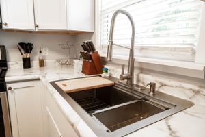 Modern white kitchen with stainless steel sink and pull-down faucet near window.