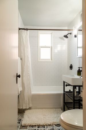 Clean white bathroom with subway tile, window, and patterned floor tiles.