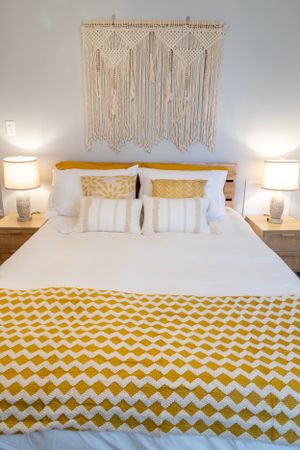 Clean white bedroom with yellow chevron blanket and handwoven macrame wall hanging.