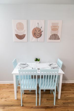 White dining table with light blue chairs and minimalist abstract art prints on the wall.