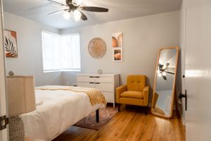 Airy bedroom with hardwood floors, ceiling fan, and yellow accent chair.