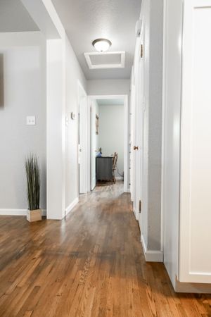 Modern hallway with hardwood floors, white walls and ceiling mounted light fixtures.