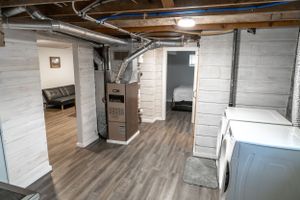 Finished basement space with exposed ceiling beams, white painted walls and wood laminate flooring.