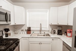 Small U-shaped kitchen with white cabinets, gas stove, and microwave above.