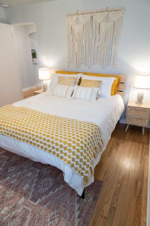 Bright bedroom featuring white linens, yellow chevron throw, and bohemian macrame wall decor.