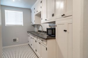 Galley kitchen with white cabinets, black appliances and checkered floor pattern.