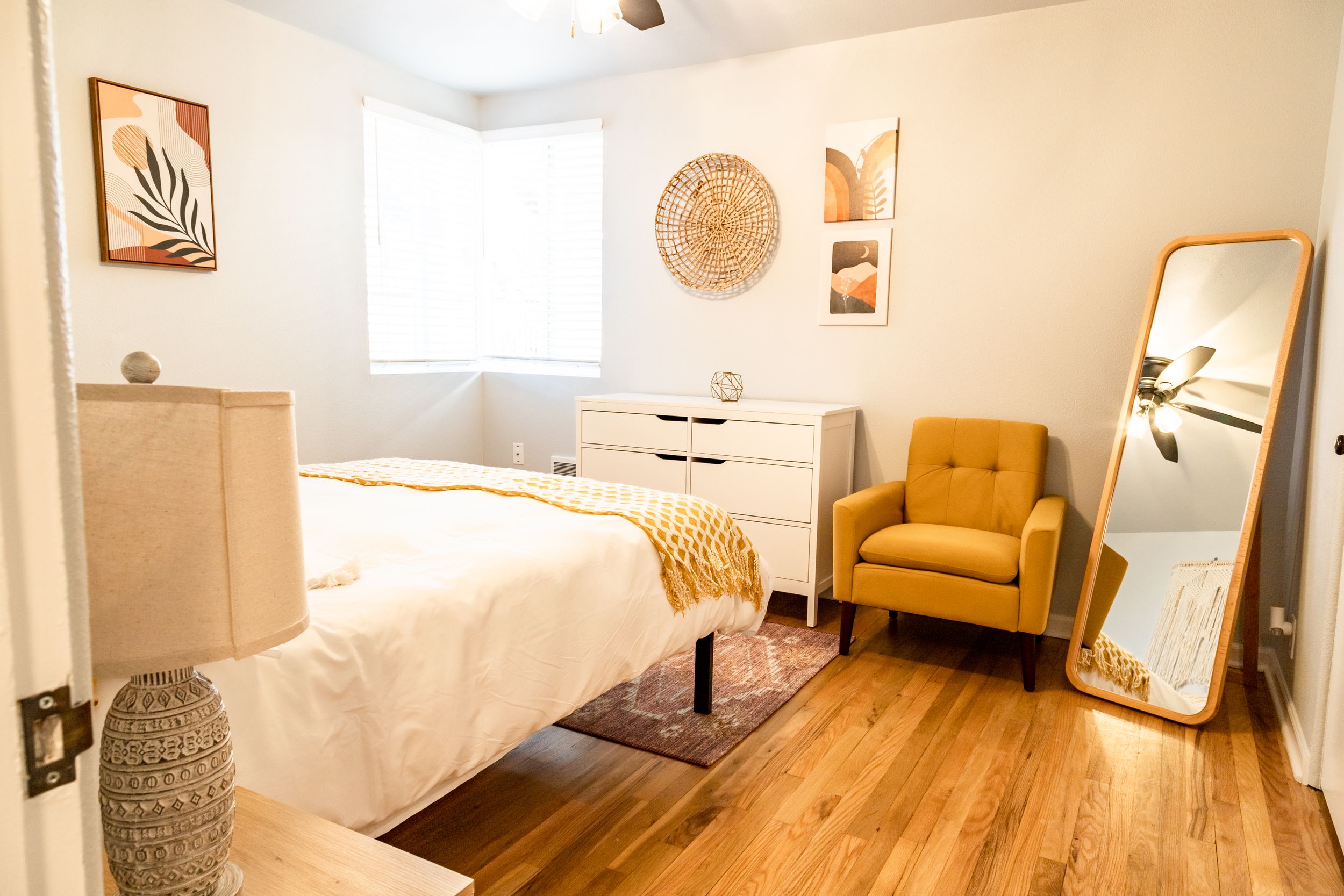 Bright bedroom featuring mustard accent chair, full-length mirror, and minimalist decor.