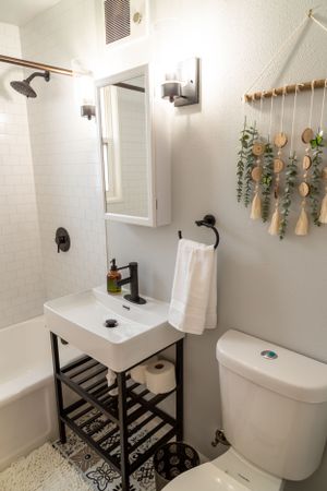 Compact bathroom featuring black metal vanity, white tile, and decorative wall hanging.