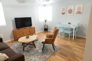 Cozy living room with brown leather chair, TV on wooden stand, and dining area with blue chairs.