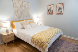Bedroom with white bedding, yellow geometric throw, and macrame wall hanging above the headboard.