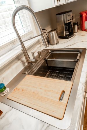 Close-up of large kitchen sink with wooden cutting board and high-arch faucet.