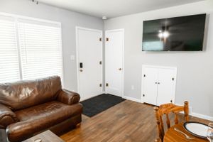 Living space with leather couch, wall-mounted TV, and wooden dining chair on hardwood floors.