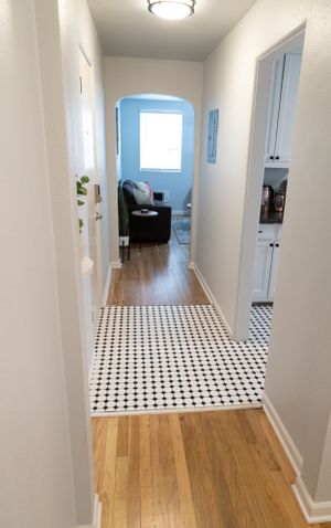 Hallway with geometric tile flooring transitioning to hardwood and white walls with arched doorway.