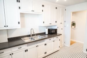 Modern white kitchen with black granite countertops and classic cabinet hardware facing a geometric tile floor.