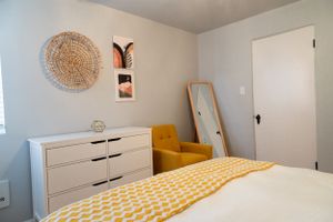 Bedroom corner with yellow armchair, white dresser, and decorative wall art.