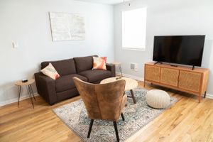 Contemporary living room with brown sofa, wooden media console, and coral accent pillow.