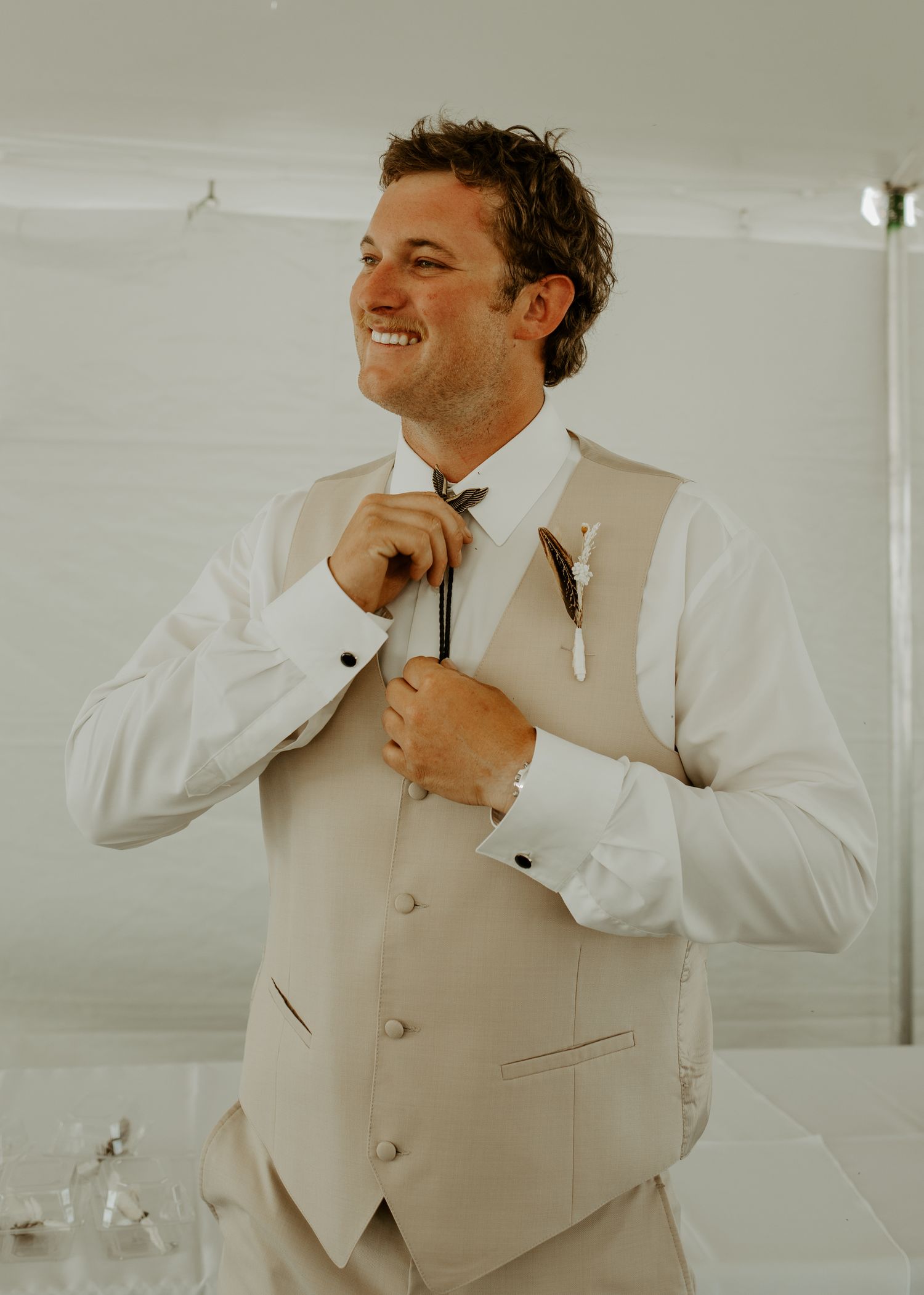 Person smiling while adjusting formal tie wearing light colored vest and white shirt.