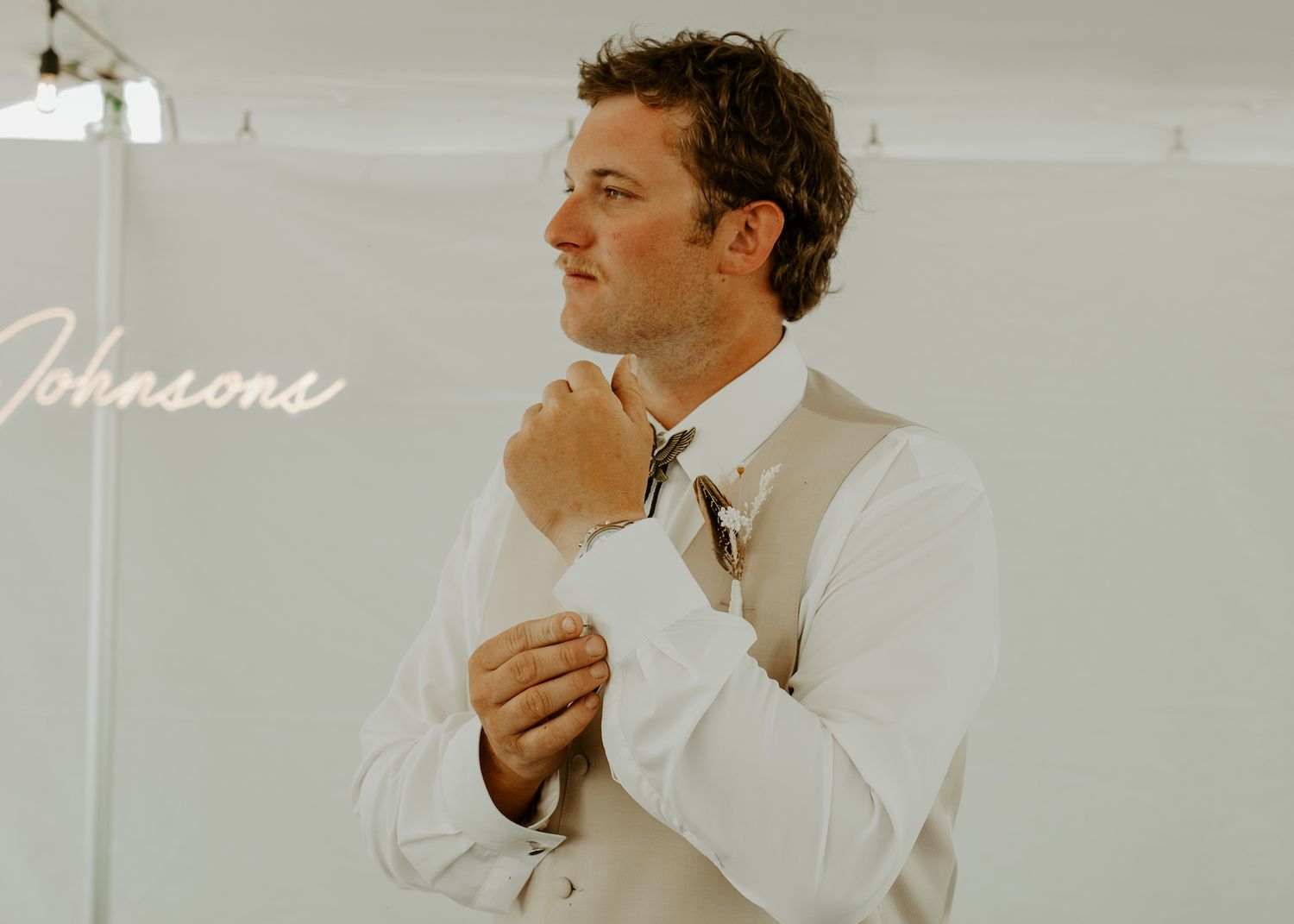 Person in beige vest and white shirt adjusts collar during wedding preparations.