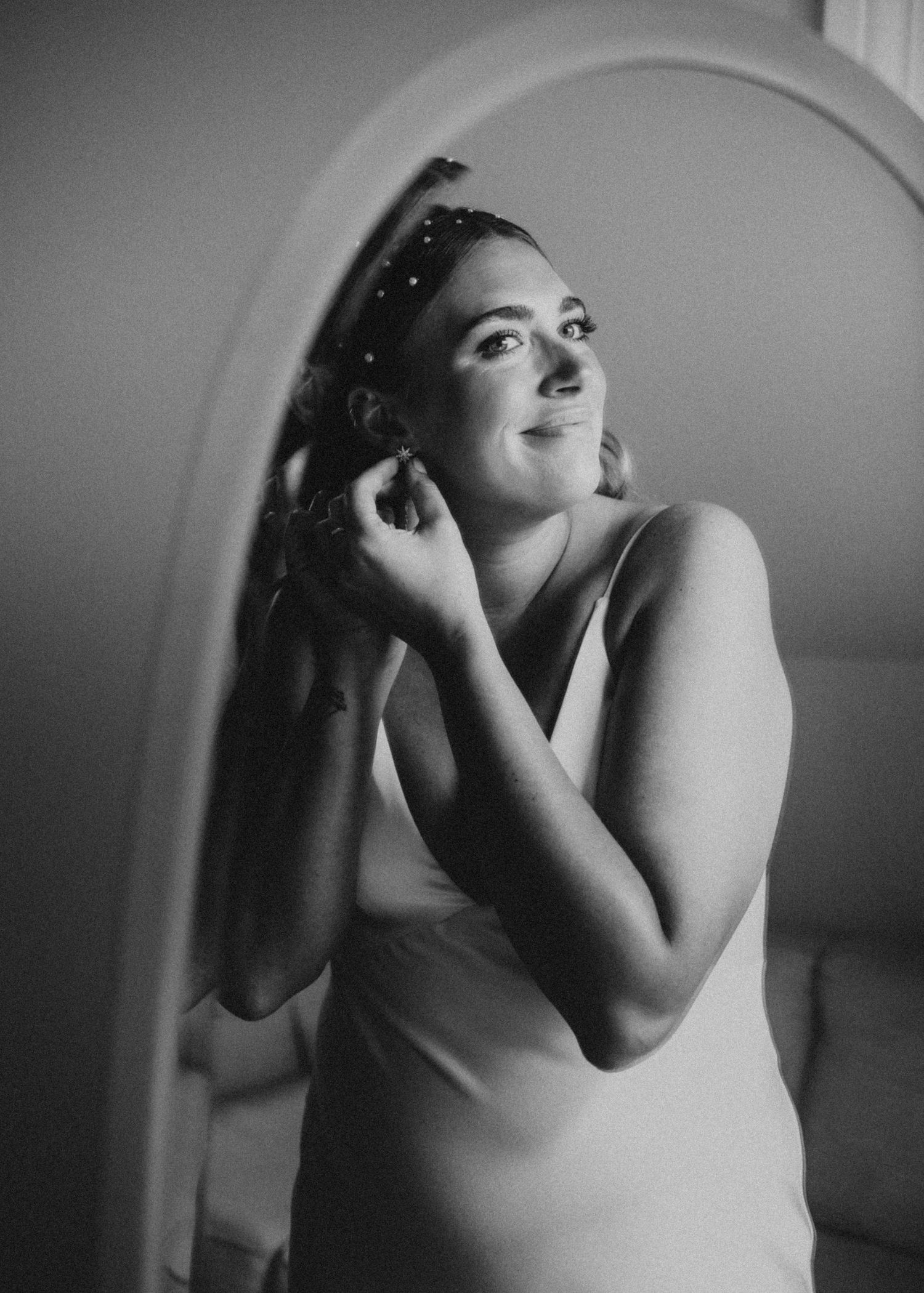 Black and white portrait through arched mirror during wedding preparations.