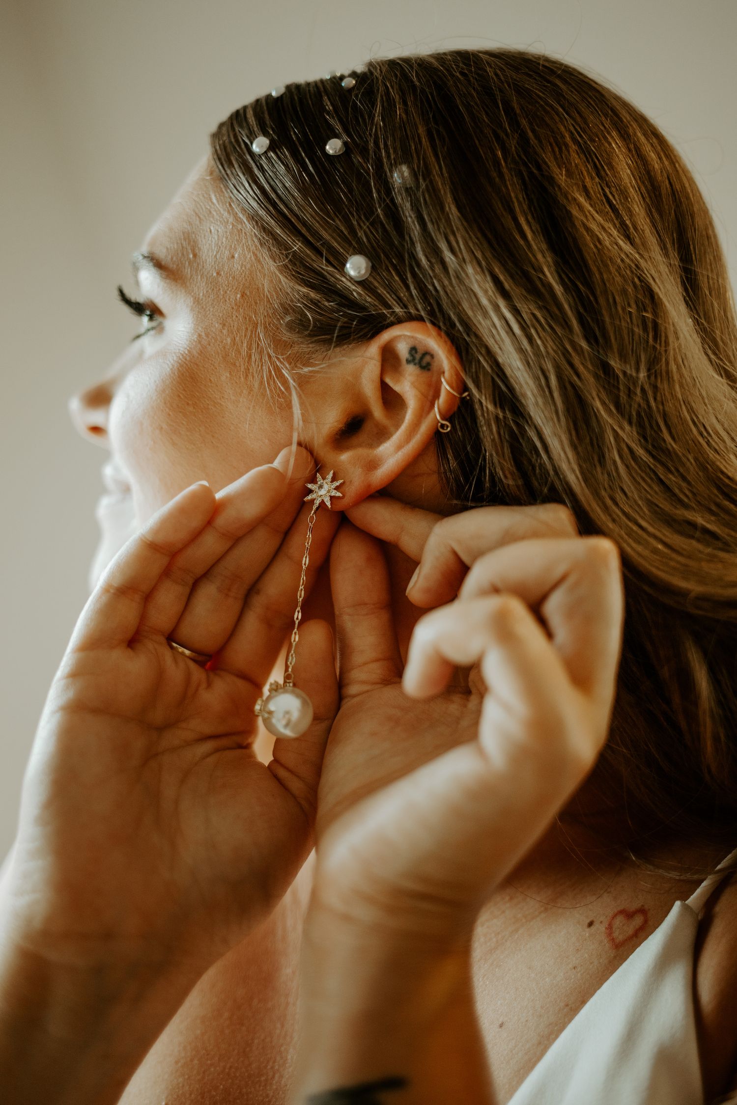 Close-up shot showing hands putting on elegant pearl and floral bridal earrings.