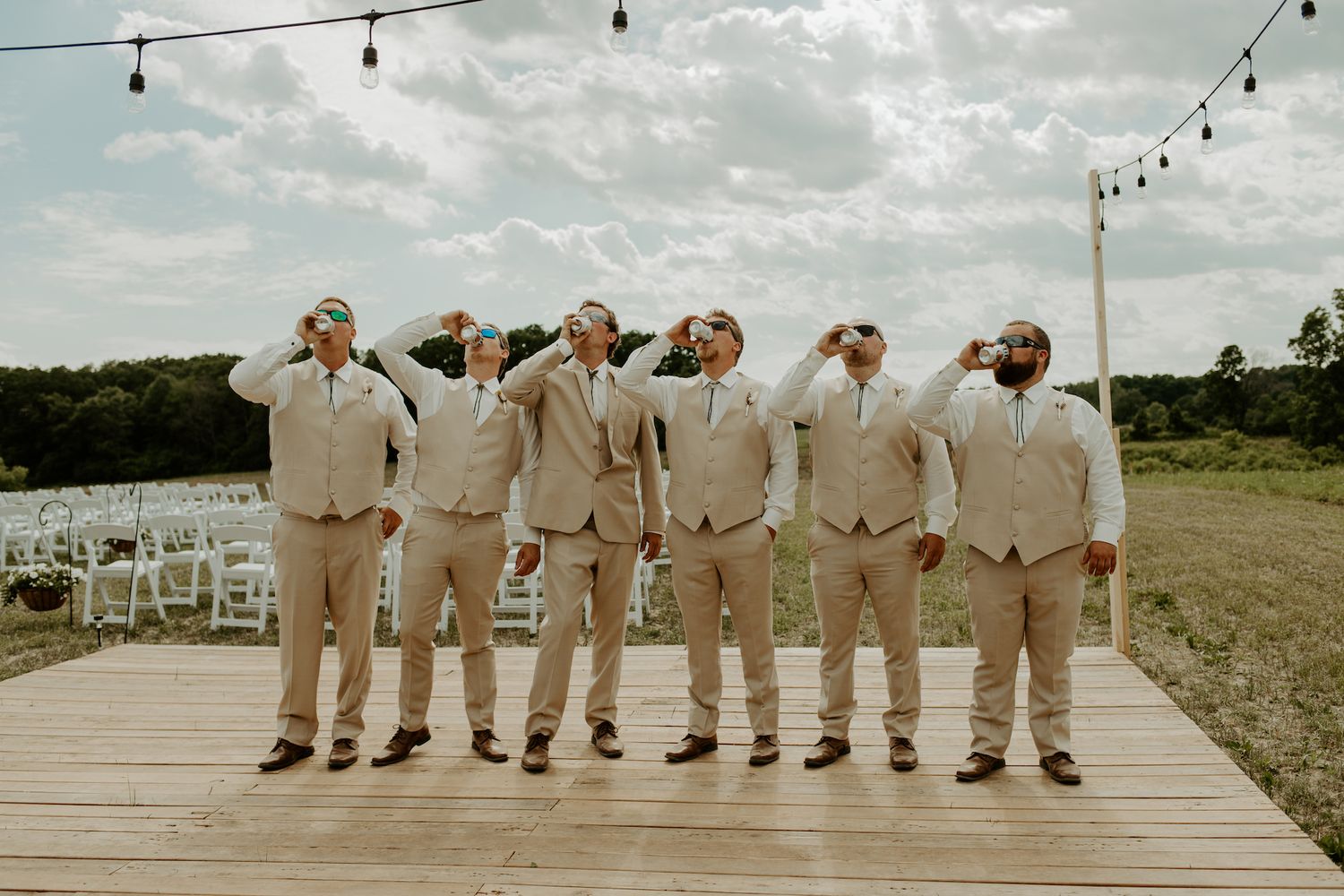 Groomsmen in beige suits posing playfully on outdoor wooden deck.